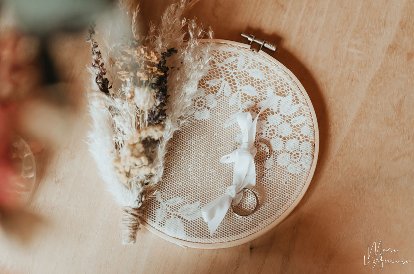 Idée d'élopement ou mariage intime : alliances et fleurs séchées sur un cerceau de dentelle par Marie l'Amuse photographe