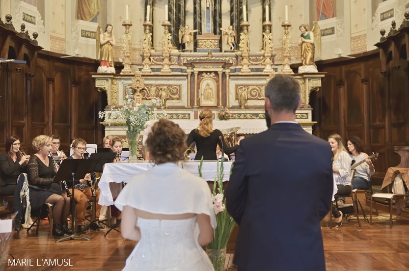 Mariage, Cérémonie, Les époux de dos regardent la fanfare de Vailly jouer à l'église, Vailly Haute Savoie -2019, Photographe Marie l'Amuse
