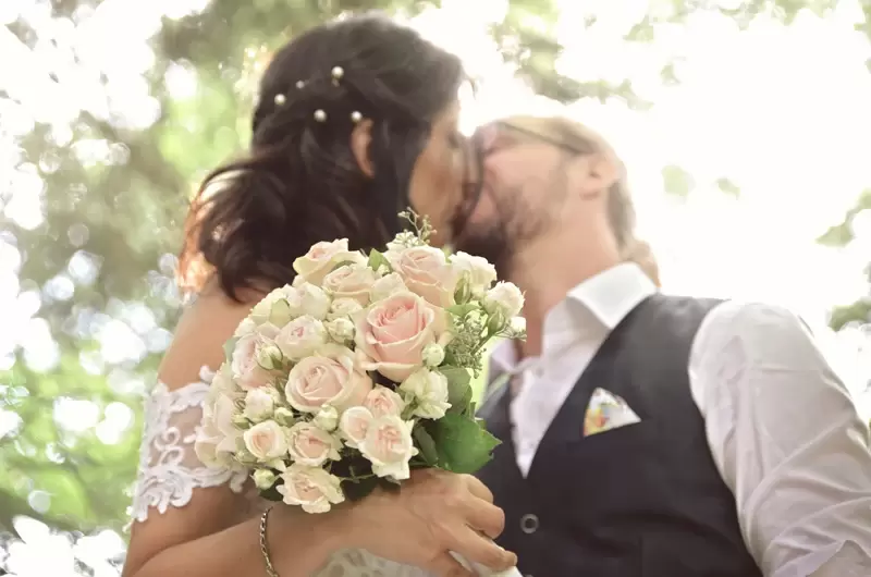 Les mariés s'embrassent derrière le bouquet fait de roses lors de la réception à Larringes