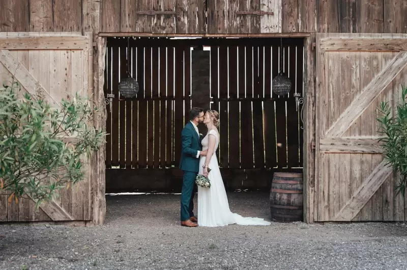 First look du couple qui s'embrasse devant la grange en bois du Château de Morgenex en Savoie
