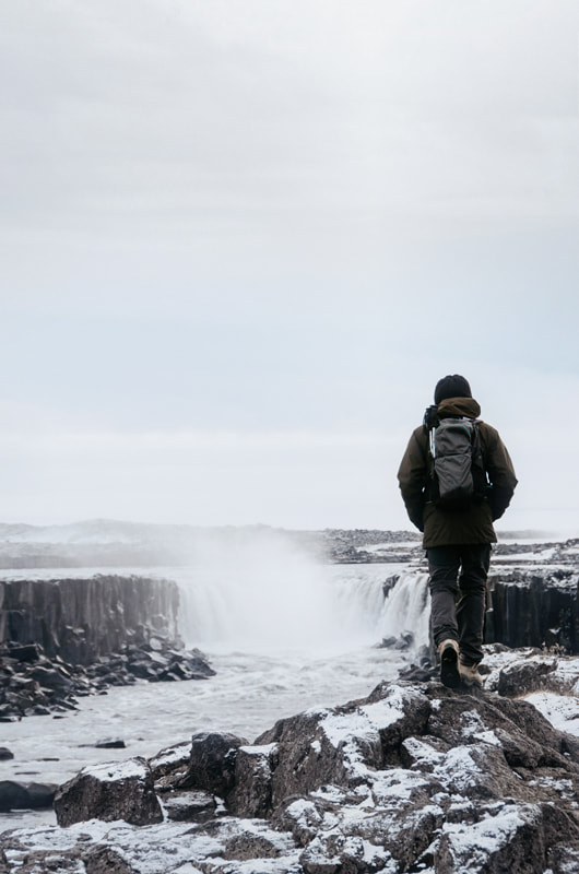Un homme en randonnée en hiver en Islande à la cascade Dettifoss pour un élopement