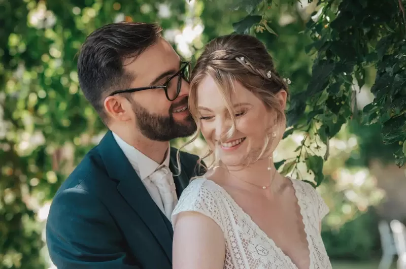 Le mari murmure à l'oreille de sa femme sous les arbres en Savoie durant la séance photo de mariage
