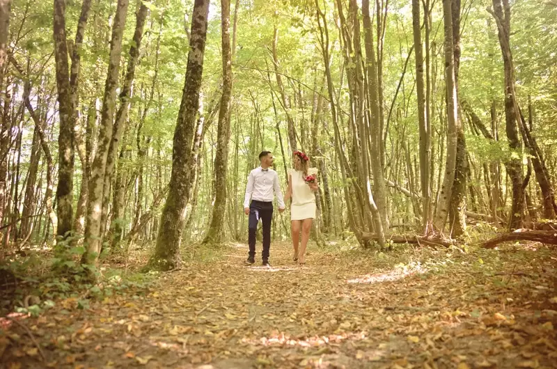 Le couple marche dans la forêt en tenue de mariés lors des photos de leur mariage à Genève
