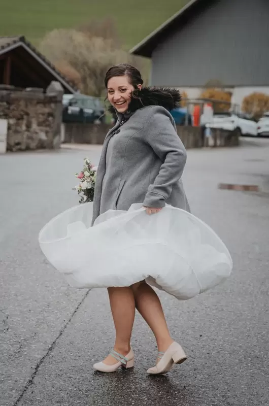 Lors d'un mariage par mauvais temps en Haute-Savoie, une photo originale de la mariée qui sourit en marchant sous la pluie