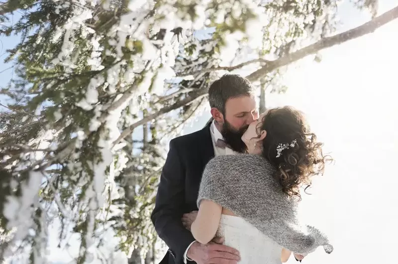 Un couple s'embrasse sous les sapins enneigés en séance day after en montagne en hiver
