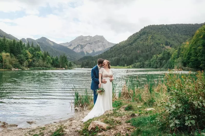 Elopement en Haute-Savoie, le couple en tenue de mariés s'embrasse devant le lac de Vallon
