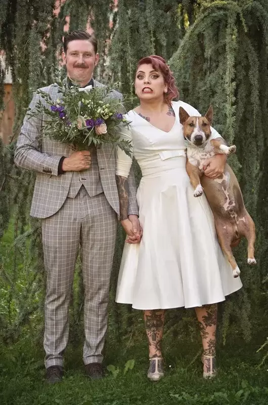 Un couple original avec des tatouages fait des grimaces avec leur chien le jour de leur elopement