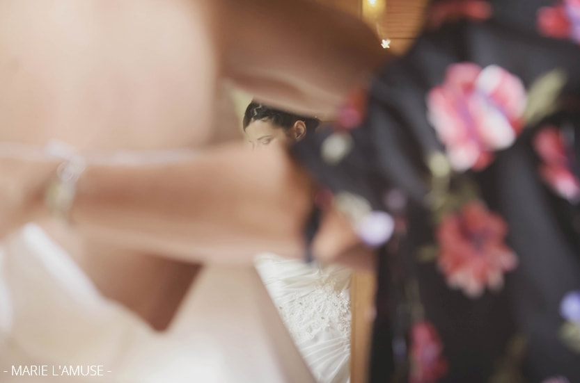 Préparatifs : dans le miroir, reflet de la mariée qui baisse le regard, sa mère l'aide à mettre sa robe. Mariage, Bellevaux, Haute-Savoie.