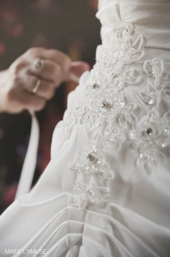 Préparatifs : gros plan sur la dentelle et strass de la robe de mariée blanche. Mariage, Bellevaux, Haute-Savoie.