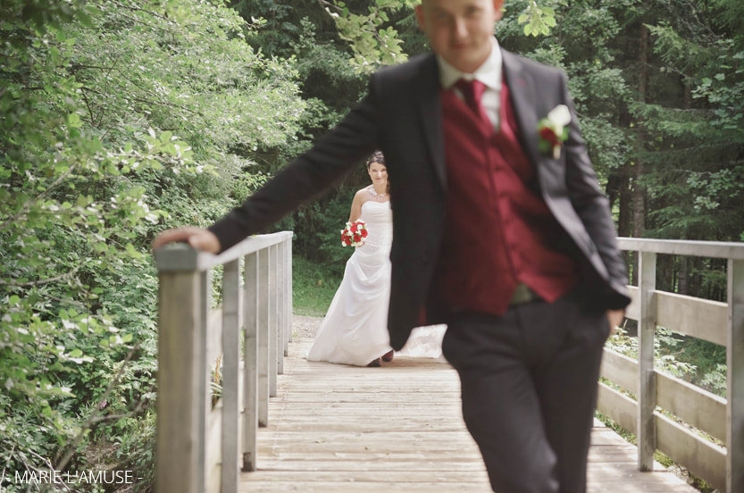 Rencontre du couple : sur un pont le marié tourne le dos à la mariée qui sourit. Mariage, lac de Vallon, Bellevaux, Haute-Savoie.