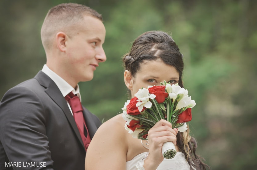 Séance photo de couple : cachée derrière son bouquet la mariée regarde la photographe. Mariage, Bellevaux, Haute-Savoie.