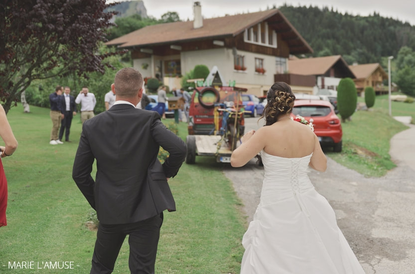 Les mariés de dos regardent la voiture balai rouge qui transporte une moto. Mariage Bellevaux, Haute-Savoie.