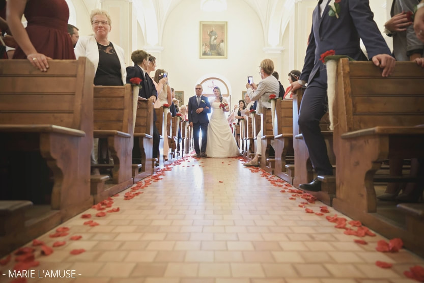 Mariage religieux, entrée de la mariée au bras de son père sur l'allée de l'église recouverte de pétales de roses rouges. Habère-Poche Vallée Verte, Haute-Savoie