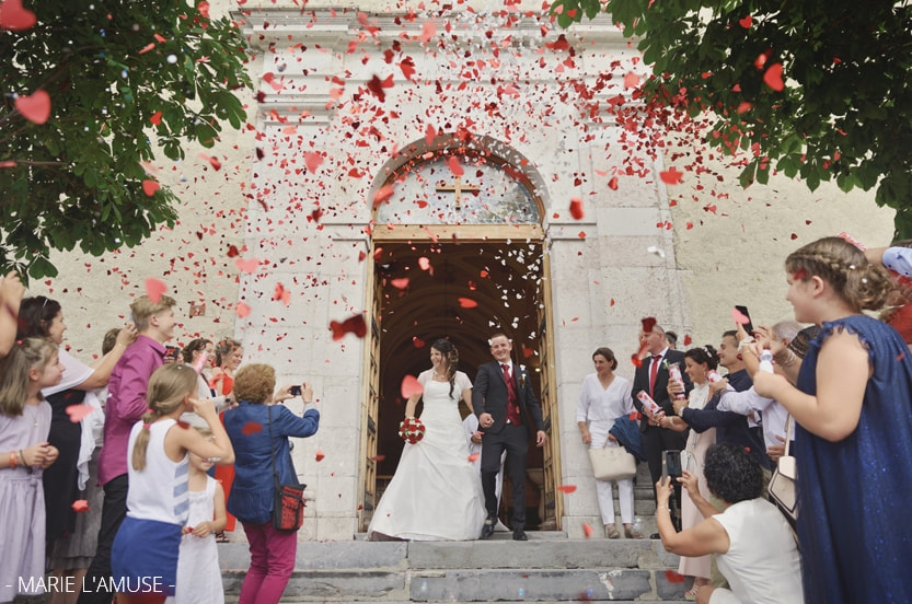 Mariage religieux, les mariés sourient en sortant de l'église, beaucoup de confettis en coeurs rouges. Habère-Poche Vallée Verte, Haute-Savoie